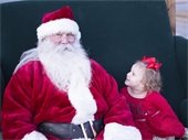 Young girl wearing red dress seated next to Santa