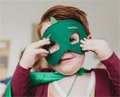 Young boy wearing green superhero mask and matching green cape