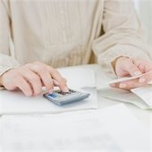 Woman's hands with calculator in one and piece of paper in the other. She appears to be paying bills.