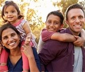 Man and woman each with one of their children on their backs smiling at the camera 