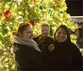 Two women and young boy smiling in front of lit Christmas tree in Downtown Mesquite