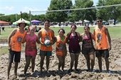 Group of friends covered in mud standing side by side, one friend holding a volleyball