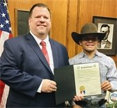 Junior bull riding champion Chris Villanueva pictured in Mayor's Bruce Archer holding proclamation. The two are pictured in the Mayor's office in front of an American flag.