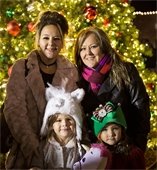 Two women and their young daughters smiling in front of Christmas tree in Downtown Mesquite