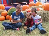 Three young kids posting together on a pumpkin patch at PumpkinFest event