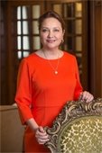 Cecilia Abbott wearing red dress posed standing behind a chair smiling at camera