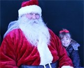 Young girl sitting next to Santa on a big chair Christmas on the Square event