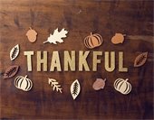 Wood table background with the word THANKFUL in gold cutout letters; decorative autumn-themed cutouts of leaves surrounding the letters